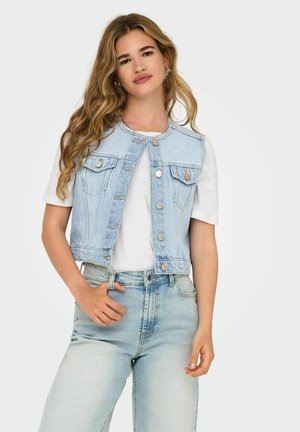 Gilet en denim bleu clair avec un design court, deux poches avant et des boutons en argent, associé à un T-shirt blanc et à un jean bleu clair.