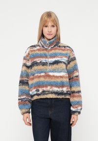 Sudadera de forro polar con cuello alto; presenta franjas horizontales multicolores en azul, marrón y crema; cierre con cremallera, textura suave y diseño corto.