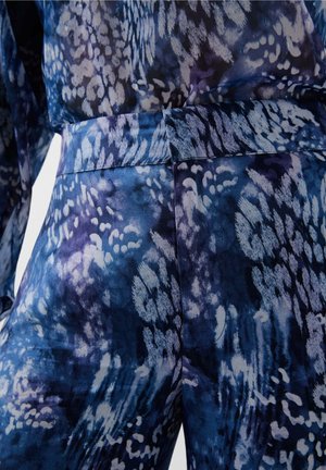 Blauwe en paarse gestreepte stof met een soepele textuur, met abstracte vormen en een aansluitende tailleband. Close-up van de details van het kledingstuk.