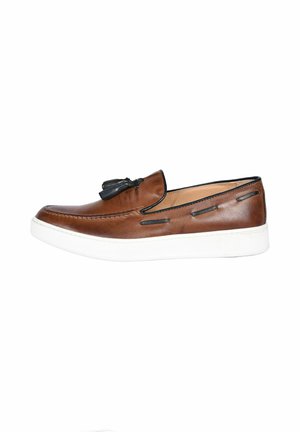Scarpa slip-on in pelle marrone con accenti neri e nappine, dotata di una suola in gomma bianca e dettagli cuciti lungo i lati.