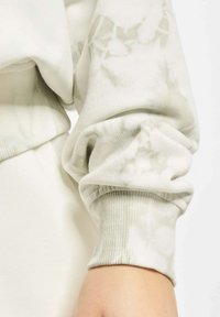 Lys grå tie-dye hettegenser med ribbede mansjetter. Stoffet ser mykt ut med en jevn tekstur, og har et avslappet design med elastiske ermer.