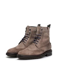 Bottes chelsea en daim marron avec des détails en brogue décoratifs, des lacets bleu foncé, des œillets en métal et un talon empilé.