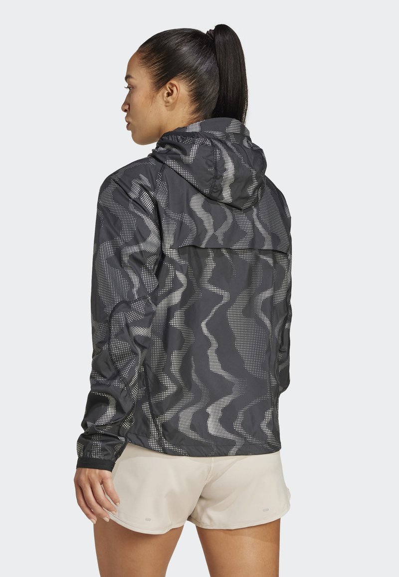 Schwarze und graue Kapuzenjacke mit Wellenmuster, leichtes Material, lange Ärmel und eine Reißverschlussrückentasche. Mit reflektierenden Punkten.