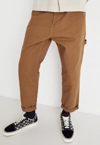 Pantaloni cargo in cotone marrone con risvolti, dotati di una tasca laterale. Abbinati a sneakers con motivo bianco e nero.