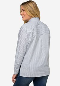 Camicia button-up a righe in blu chiaro e bianco, con una piega sul retro e logo sulla spalla. Realizzata in tessuto tessuto, maniche lunghe.