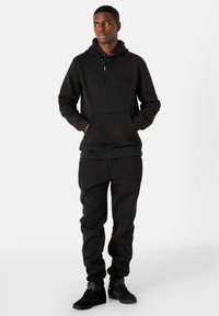 Completo felpa con cappuccio nero realizzato in tessuto morbido. Il cappuccio presenta testo in rilievo e tasca stile kangaroo; i pantaloni hanno una vita elastica e polsini.