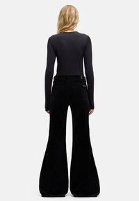 Top nero a maniche lunghe abbinato a pantaloni neri a gamba larga in velluto a coste. L'outfit presenta un design aderente e una texture liscia.