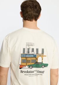 Crème-kleurig katoenen T-shirt met een grafiek van een cocktaillounge en vintage auto’s in oranje en groen. De tekst luidt "Revolution™ Vintage."