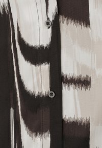 Close-up of black, white, and beige abstract patterned fabric with two small black buttons sewn on a vertical strip.