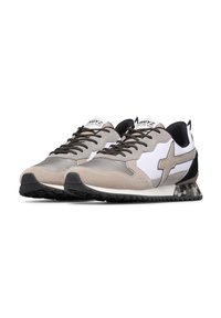 Un paio di scarpe da ginnastica atletiche beige, bianche e nere con lacci neri, un logo a stella sul lato e suole a cuneo con motivo mimetico.