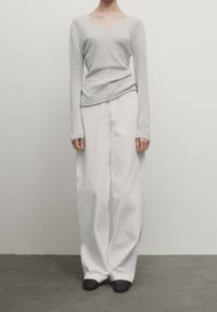 Light gray, long-sleeve, V-neck sweater paired with loose, white trousers; flat, dark shoes complete the outfit. Simple, contemporary design.