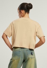 Beige t-paita, lyhyillä hihoilla ja lyhennettynä, jossa on sileä rakenne. Yhdistettynä vaalennettuihin sinisiin farkkuihin, joissa on selkeä paikka takataskussa.