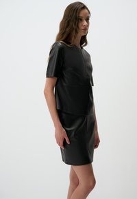 Schwarzes Lederkleid mit kurzen Ärmeln, tailliertem Oberteil und leicht ausgestelltem Rock. Glatte Textur mit subtilen Nahtdetails.