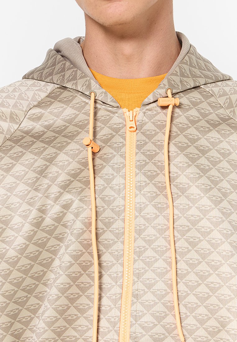 Felpa con cappuccio beige a motivi, con un design a diamante testurizzato, dotata di chiusura frontale con zip e lacci arancioni. Lo strato interno è giallo.