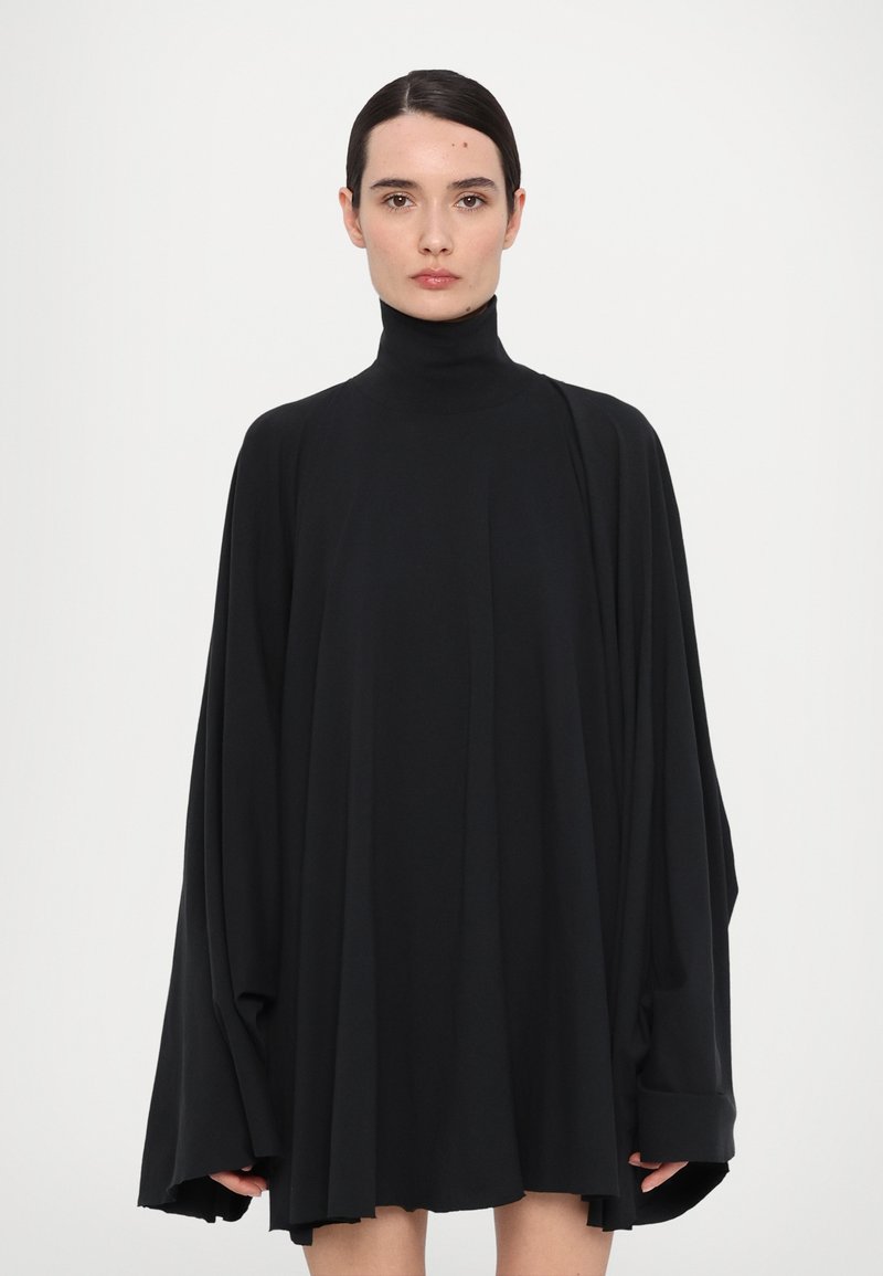 Mustassa ylisuureksi tehty pooledressissä on pitkät hihat, ja siinä on soljuva siluetti ja pehmeä materiaali, ulottuen reiden puoliväliin.