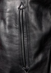 Schwarzes Leder mit einer glatten Textur. Verfügt über eine vertikale Reißverschlusstasche und ein dreieckiges Akzent über dem Reißverschluss.