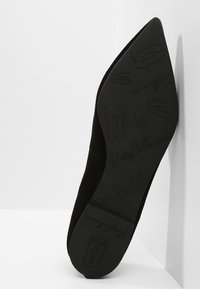 Chausson plat noir à bout pointu avec des motifs de ballerine en relief et le texte "Pretty Ballerinas" sur la semelle.