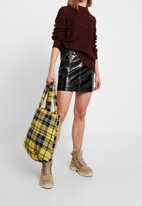 Jersey de punto de cable burdeos, minifalda de cuero negro brillo con detalle en la costura lateral, bolso de cuadros amarillo, botas beige con cordones.
