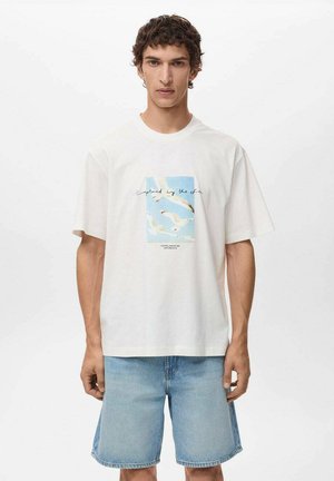 White cotton t-shirt featuring a blue and white graphic of seagulls with the text "captured by the sea." Paired with light blue denim shorts.