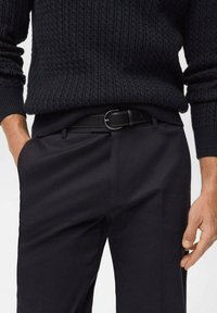 Black knitted sweater with a textured, ribbed design paired with tailored black trousers and a black leather belt featuring a round metal buckle.