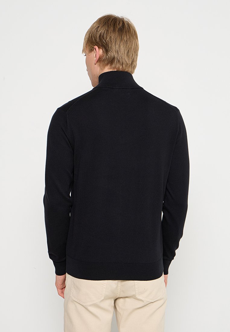 Maglione nero lavorato a maglia con colletto alto, maniche lunghe e polsini a costine. Texture liscia, design aderente e stile minimalista.