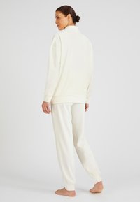 Conjunto de loungewear blanco que incluye una parte superior de corte relajado con cremallera y pantalones elásticos con puños. La tela parece suave y tiene un acabado texturizado.