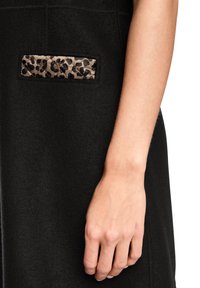 Schwarzes Fleece-Kleidungsstück mit einer gesteppte Tasche im Leopardenmuster. Glatte Textur, figurbetonte Form und sichtbare Nähte verbessern das Design.