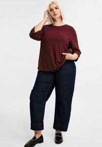 Bordeaux ribbel bovenstuk met 3/4 mouwen, gecombineerd met donkerblauwe wijde denim broek met zichtbare stiksels, en zwarte loafers met kettingdetail.