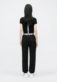 Čierne priliehavé tričko s krátkym rukávom a vertikálnym logom na chrbte. Kombinované s voľnými čiernymi teplákmi a bielymi teniskami.