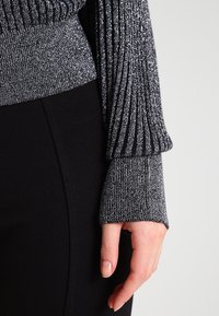 Svart ribbad topp med silvermetalltrådar, med långa, figurnära ärmar och en texturerad yta, kombinerad med en enfärgad svart nederdel.