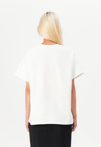 White cotton T-shirt with short sleeves and a crew neckline, featuring a relaxed fit and smooth texture. Back view shows simplicity in design.