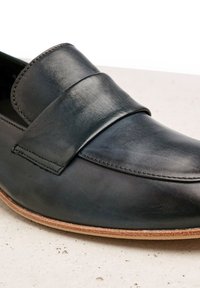 Mocasines de cuero negro con una tirante ancha en la parte superior, textura suave y una suela de goma de color claro.