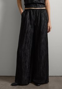 Pantalones negros de pierna ancha hechos de una tela texturizada con un aspecto arrugado, que cuentan con una cinturilla elástica y bolsillos laterales.