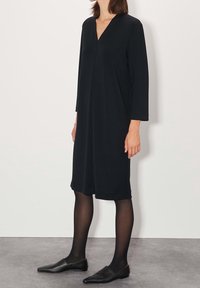 Černé šaty s dlouhým rukávem a výstřihem do V, dosahující do poloviny lýtek. Vyrobené z měkké látky, mají volný střih a minimalistický design.