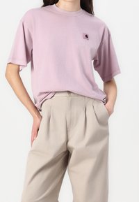 Light pink cotton t-shirt with short sleeves and a crew neck, featuring a small square logo patch on the chest, paired with beige pleated trousers.