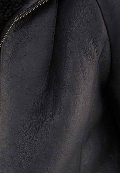 Primo piano di una giacca in pelle nera con texture, con una cerniera metallica parzialmente visibile sul lato superiore sinistro.