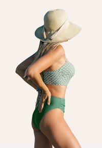 Zielony bikini z wysokim stanem i geometrycznym wzorem na górze, w połączeniu z szerokim kapeluszem słomkowym z akcentem w postaci wstążki. Subtelnie teksturowane materiały.