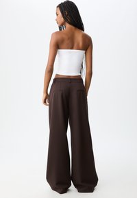Witte strapless top gecombineerd met bruine wijde broek met achterzakken en een gladde, textuurachtige afwerking.