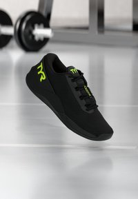 Zapato deportivo negro hecho de material de malla, con una superficie texturizada, acentos verdes y un diseño de cordones con un cuello acolchado.