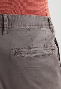 Grå bomullsshorts med en platt bakficka, lättviktsmaterial och en slät yta. Midjebandet har en bälteshäll.