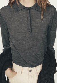 Ciemnoszara koszulka polo z długim rękawem, kołnierzykiem, trzema guzikami z przodu i fakturowanym wykończeniem, zestawiona z jasnymi spodniami sztruksowymi.