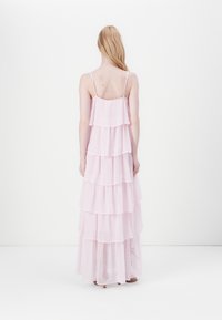 Hosszú, rózsaszín ruha réteges fodrokkal, vékony pántokkal és könnyű anyagból. A kialakítás laza siluettet és áttetsző, rétegzett textúrát mutat.