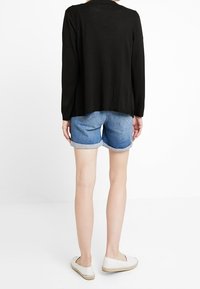 Black long-sleeve cardigan, soft fabric, slightly loose fit, paired with light blue denim shorts and white espadrilles. Simple, casual outfit.