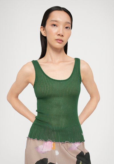 Grünes, geripptes Tanktop mit scoopförmigem Ausschnitt und gewelltem Saum. Hat ein enganliegendes Design und eine feine Textur. Getragen mit einem gemusterten Rock.