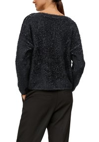 Czarny, puszysty sweter o fakturowanym wykończeniu oraz szerokim dekolcie, w połączeniu z czarnymi spodniami. Luźny krój, casualowy styl, brak widocznych zapięć.
