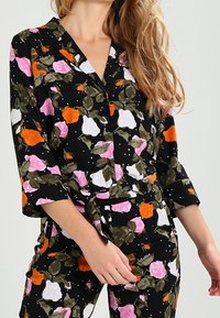 Ensemble de pyjama floral avec un fond noir orné de roses roses, blanches et orange, de feuilles vertes, et une coupe décontractée avec des manches trois-quarts.