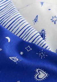 Tessuto di cotone blu con motivi stampati bianchi che presentano cuori, stelle e diamanti. È visibile un tessuto bianco separato con strisce blu.