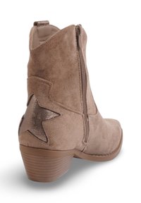 Botte de cheville en daim marron avec une fermeture éclair sur le côté, dotée d'une étoile métallique sur le talon et d'un talon bloc texturé.