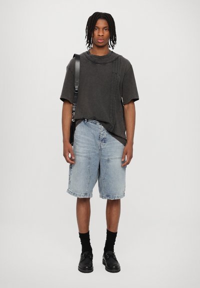 Black oversized t-shirt with curved neckline and side details, paired with light blue denim shorts. Worn with black socks and shoes.