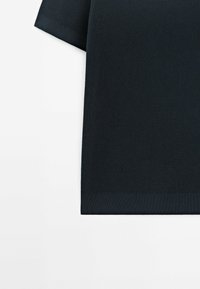 Haut noir en maille à manches courtes avec tissu texturé et ourlet côtelé sur fond blanc.